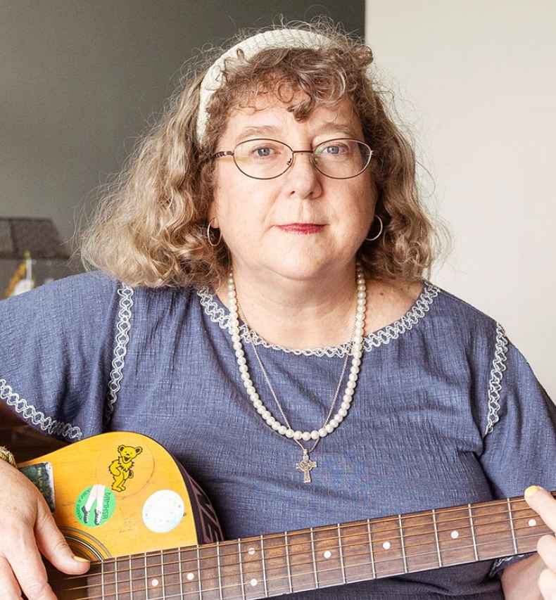 Participant Mary - person with wavy grey hair holding a guitar