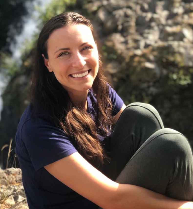 Participant Natalia - person with long brown hair sitting on a large rock outside