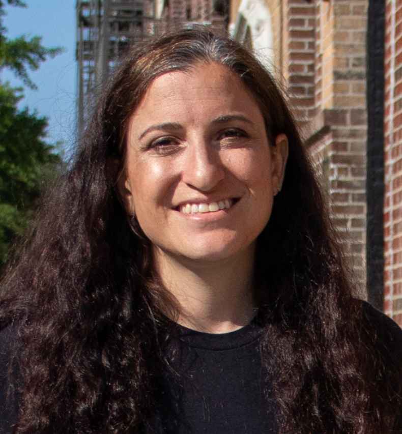 Participant Michelle - person with long, dark, wavy hair outside in front of a brick building