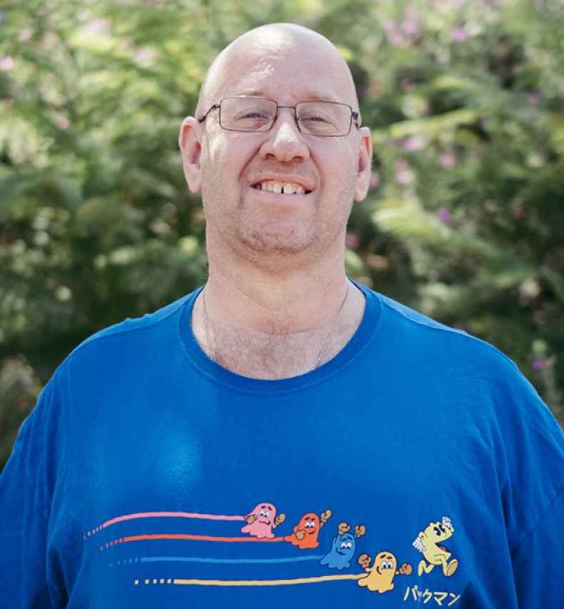 Deconstructing Stigma participant Ori - Person in blue shirt stands outside greenery behind