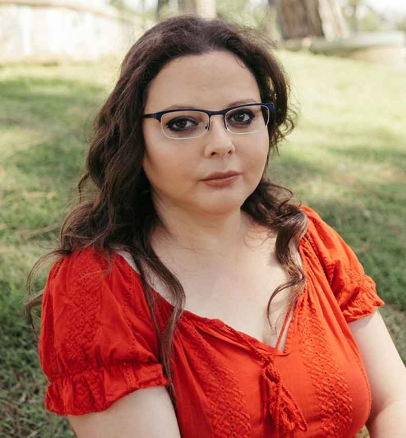 Deconstructing Stigma participant Shlomit-Coana - person in red dress and glasses sits outside