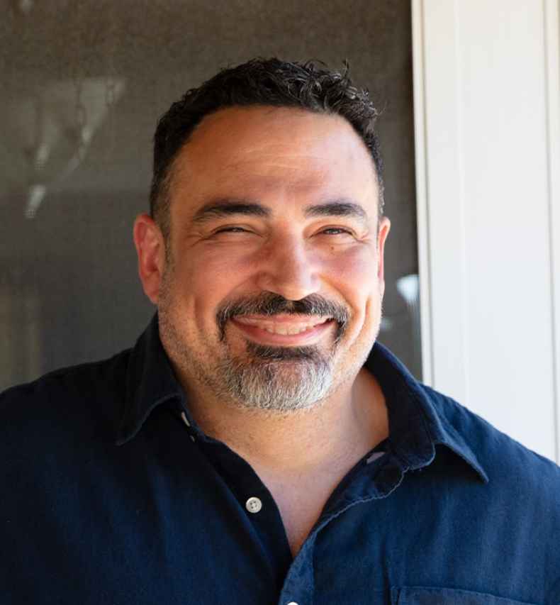 Participant Wayne - person with short dark hair smiling outside a door