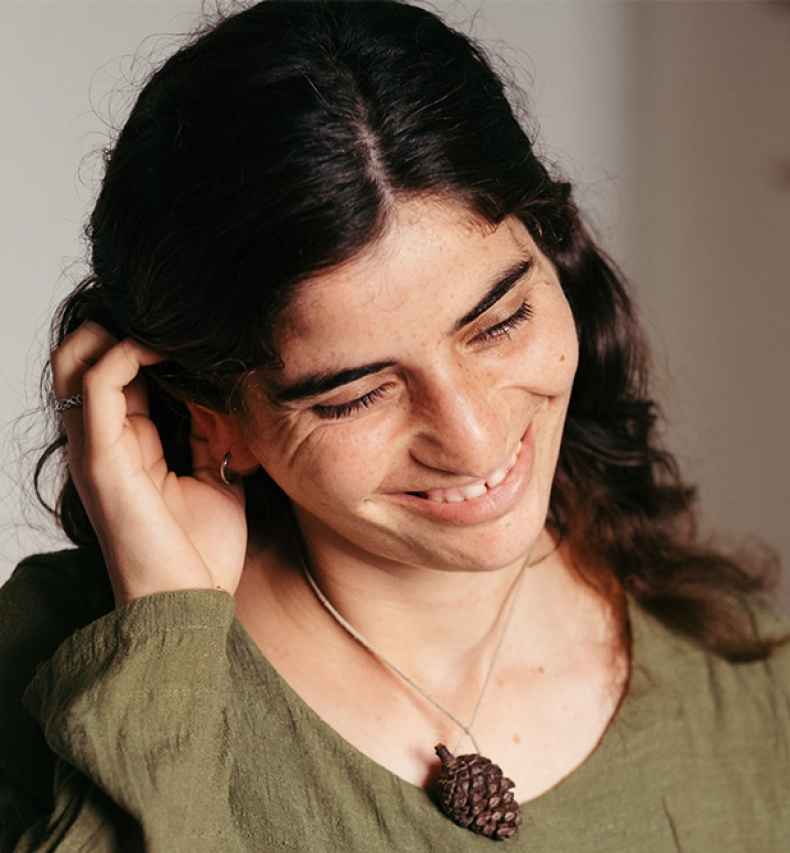 Deconstructing Stigma participant Yaqueen - portrait of person not looking up wearing green shirt and pinecone necklace