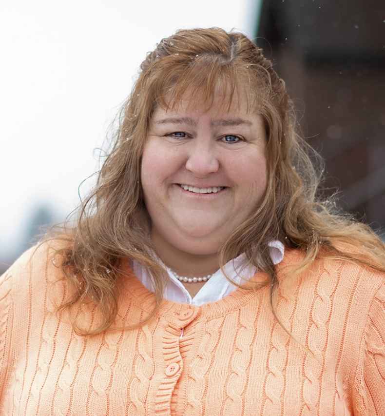 Participant Jodi - person with long auburn hair smiling outside on stairs while snow falls