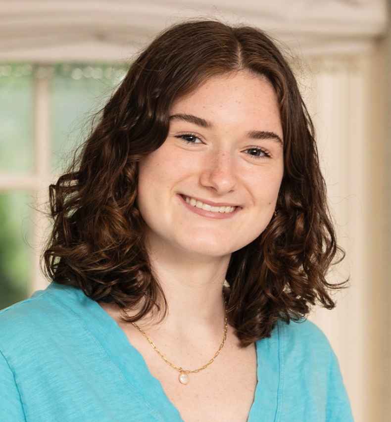 Participant Caroline - person with short brown hair smiling in front of a window and a bookshelf