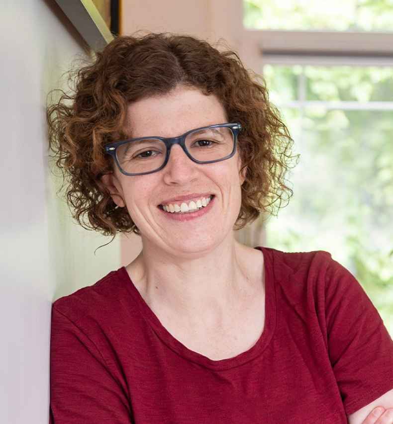 Participant Caitlin - person with short curly hair and glasses smiling