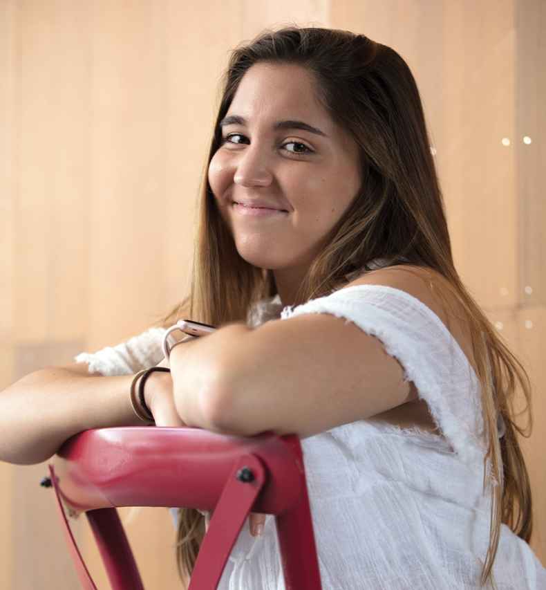 Participant Ana - person with long brown hair smiling and leaning on a red chair