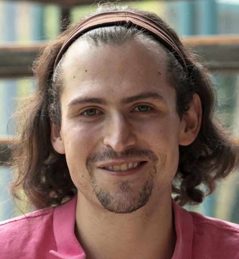Participant Joaquín - person with shoulder-length brown hair smiling in front of a large window