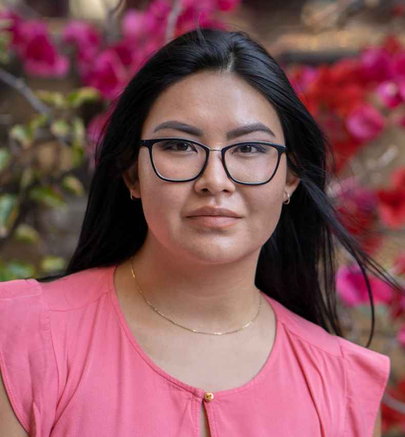 Participant Kaylee - person with long dark hair and glasses outside surrounded by pink flowers