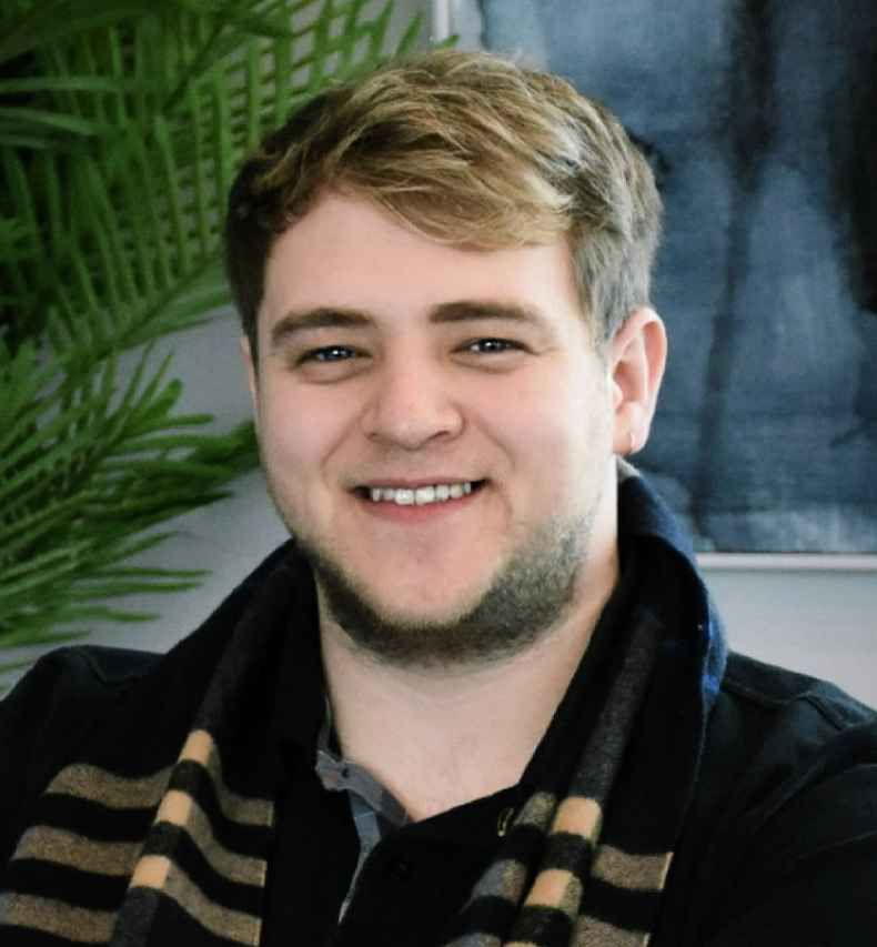 Participant Jay - person with short brown hair sitting in front of a houseplant and a painting