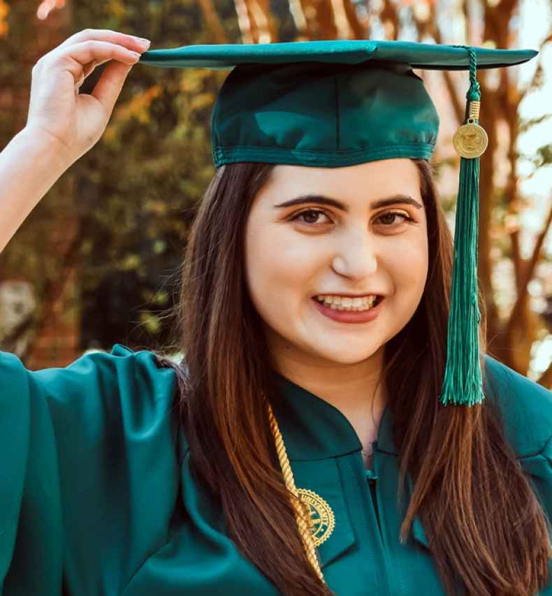 Participant Carly - person with long auburn hair smiling and wearing a green graduation cap and gown