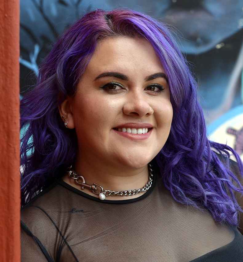 Participant Joanne - person with purple hair smiling in front of a colorfully painted wall