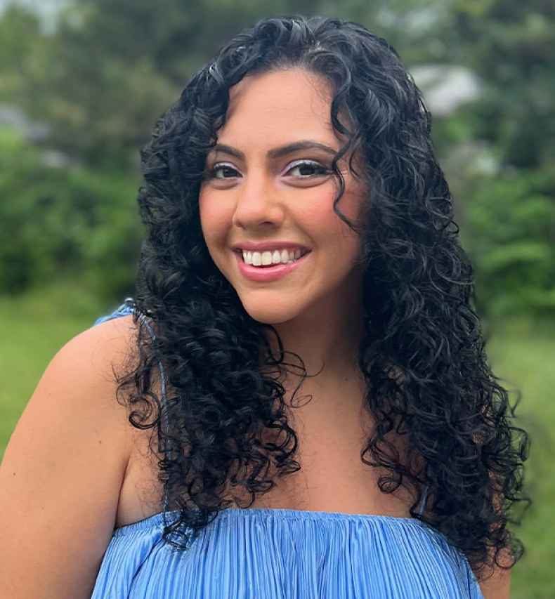Participant Irene - person with long and wavy dark hair wearing blue and smiling outside