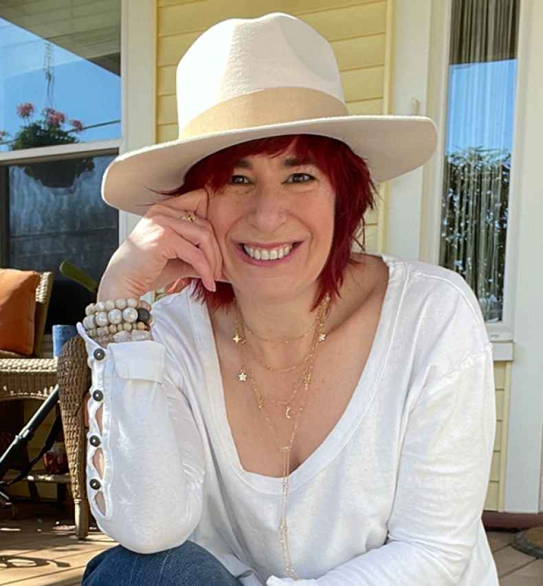 Participant Jen - person with red hair wearing a large hat smiling in front of a doorway