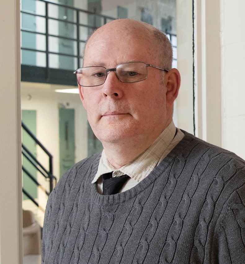 Participant John - person with glasses wearing a grey sweater in front of an office window