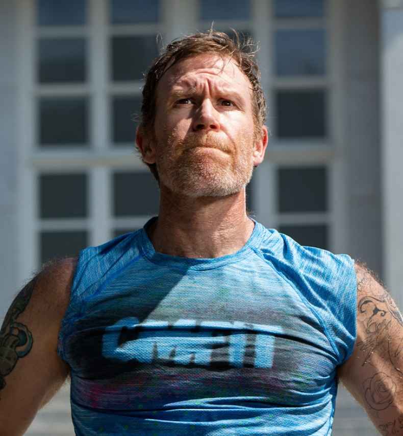 Participant Alan - person with short brown hair wearing a blue tank top standing in front of stone steps outside