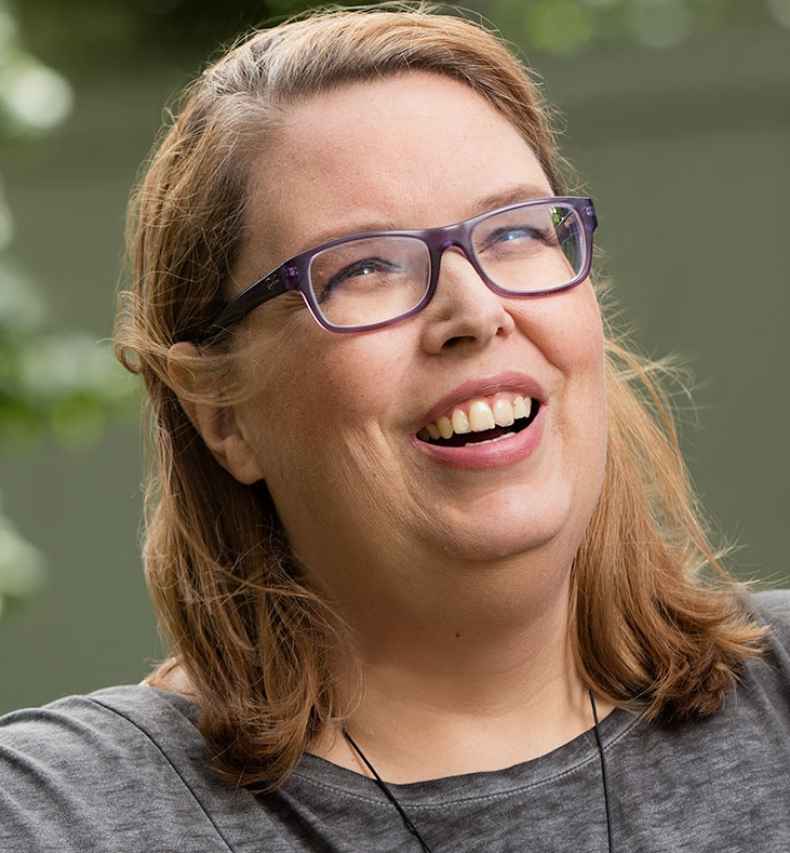 Participant Laura with blonde hair and glasses is sitting in a chair outside smiling