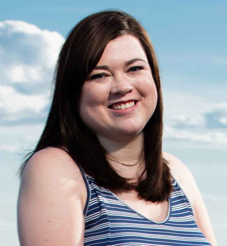 Participant Clare - person with long dark hair smiling in front of a blue sky