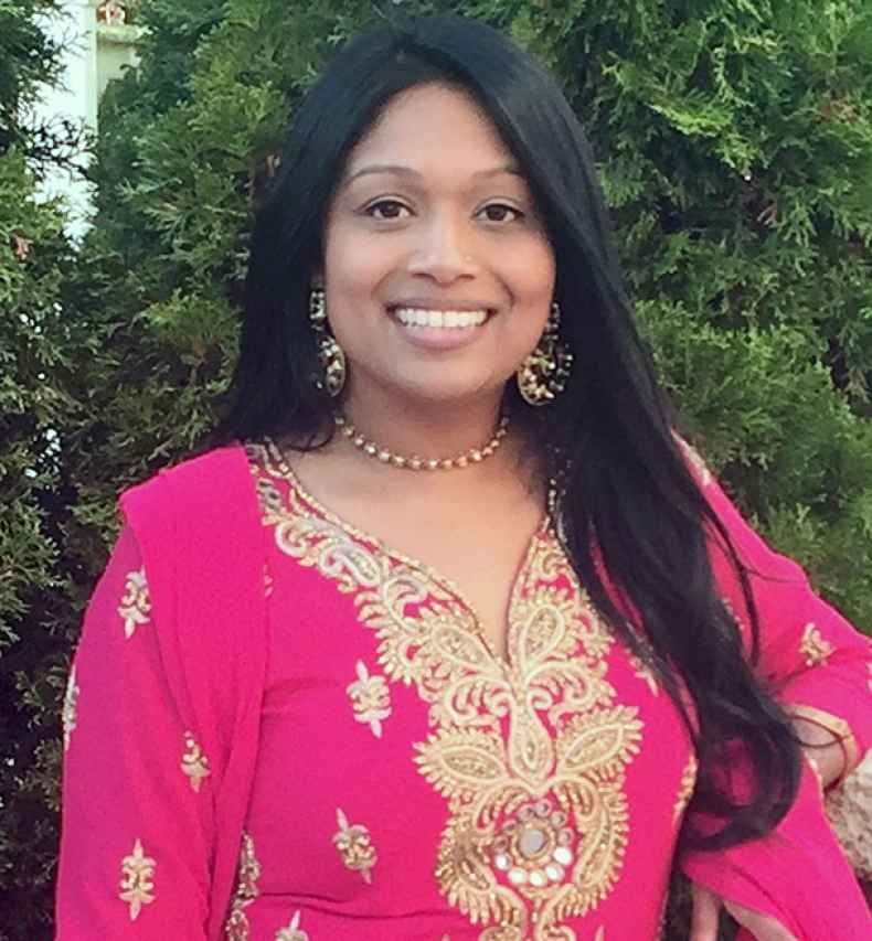 Participant Subrina - person with long dark hair wearing bright pink clothes and smiling in front of greenery