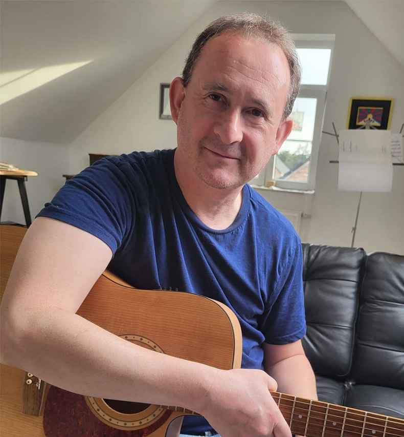Deconstructing Stigma participant Paul - person sits on couch playing guitar