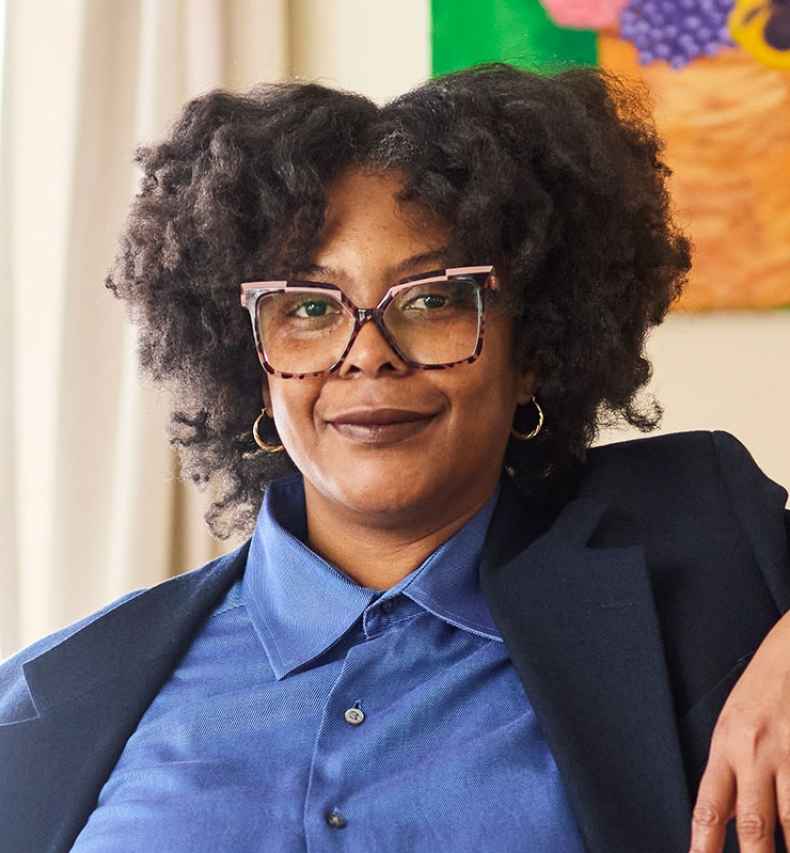 Deconstructing Stigma participant Johanne - person in blue blazer stands by bookcase