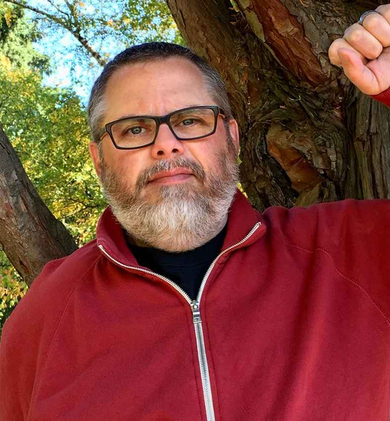 Deconstructing Stigma participant Noal - person in red zip up and glasses leans on tree