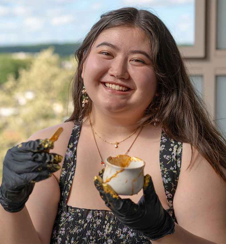 Deconstructing Stigma participant Natalie - young person holds broken cup and stick with gold paint to fix
