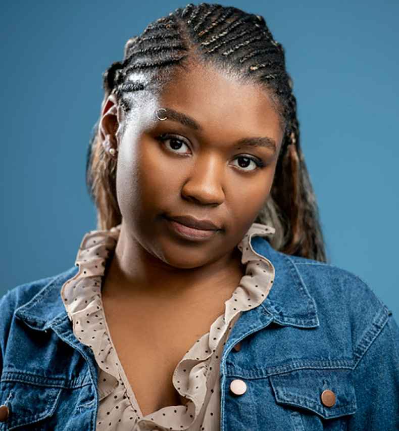 Deconstructing Stigma participant Jamorra - person with long braids poses on blue background