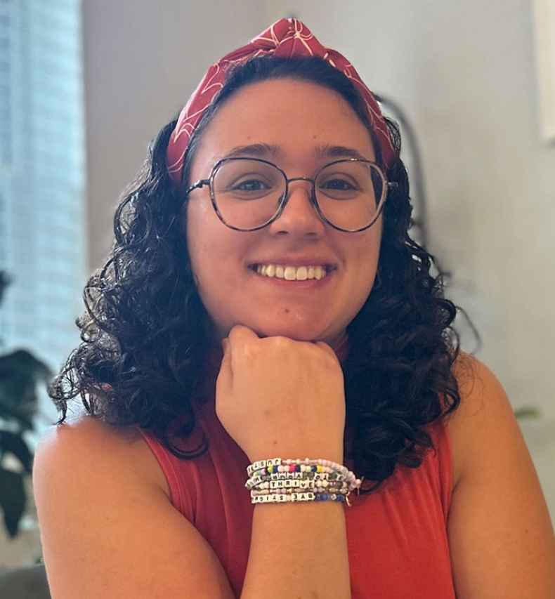 Deconstructing Stigma participant Lisa - young person in glasses and bandana sits with head perched on hand