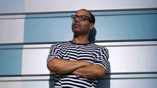Participant Richard - person with short hair and glasses in a striped shirt leaning against a blue geometric wall
