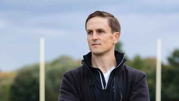 Participant Justin - person in black sweatshirt with arms crossed on a football field