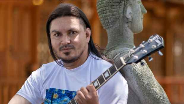 Participant Pablo - person with long dark hair holding a guitar and leaning against a statue