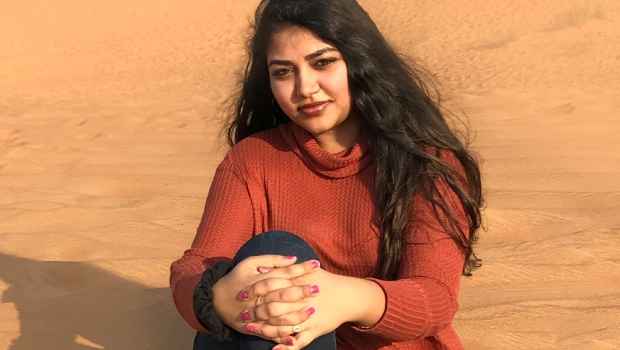 Participant Ramya - person with long dark hair in a red sweater sitting in sand