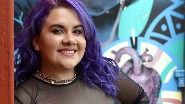 Participant Joanne - person with purple hair smiling in front of a colorfully painted wall
