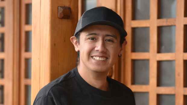 Participant Jimmy - person with short dark hair wearing a black baseball hat and smiling outside a wooden building