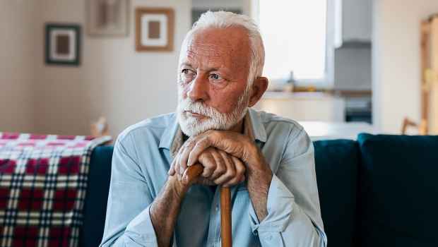 Older man on couch leans head and hands on cane