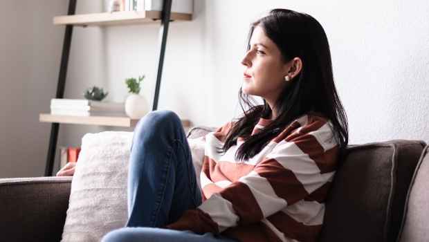 Person sits on couch with knee up looking out window