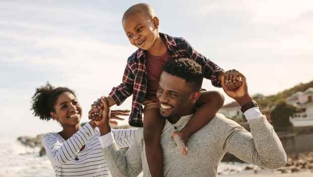 Family with kid on dad shoulders walk on beach