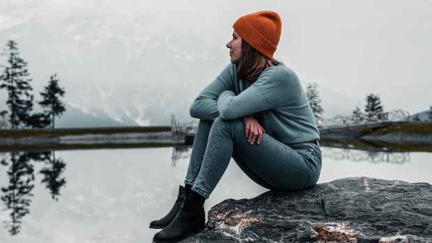 Person sits on rock looking out at lake in gray winter
