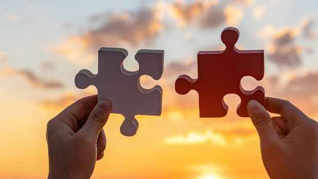 Two hands holding large jigsaw puzzle pieces in front of a sunset