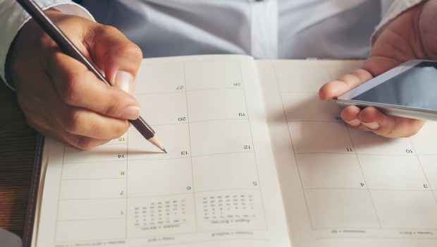 Hand holding smartphone, the other writing in calendar