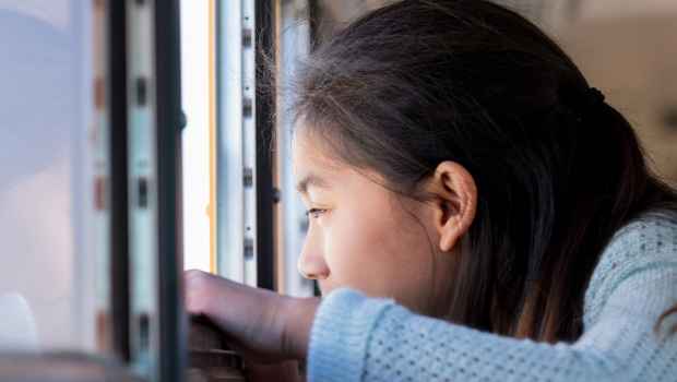 Girl with long dark hair looking out an open school bus window