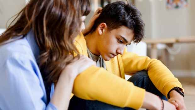 Boy sits, looking down, and a woman comforts him