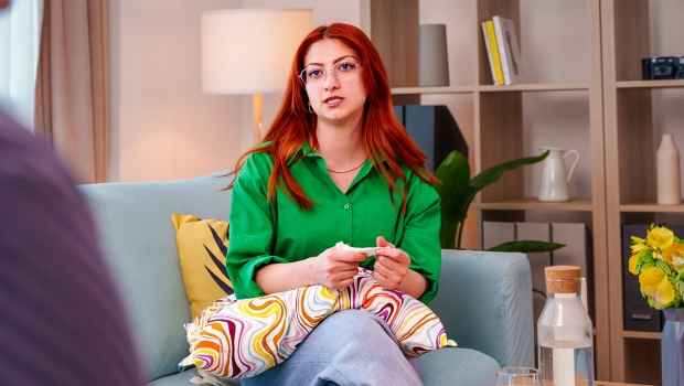 Person with bright red hair wearing a green shirt and sitting on a couch