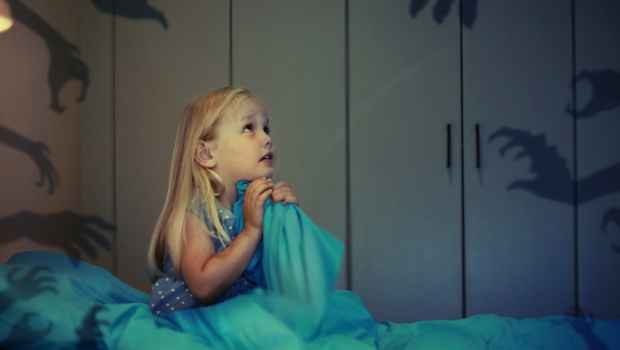 Young girl sits in bed surrounded by shadows of monsters