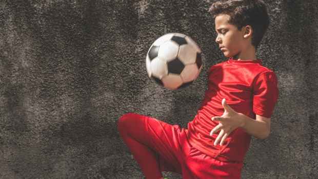 Boy in a red soccer uniform playing with a soccer ball