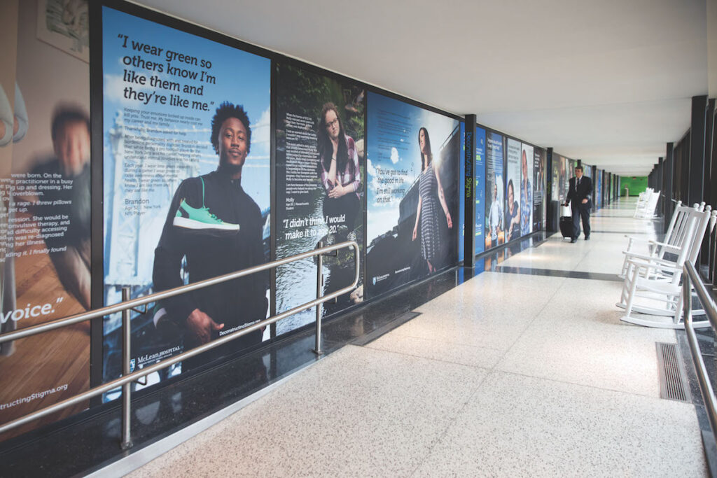 A photo gallery at the Boston Logan airport with several huge photographs and text next to each other on a long wall with people looking at the photographs.