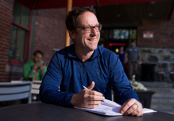 Man in blue shirt sitting at a table smiling.