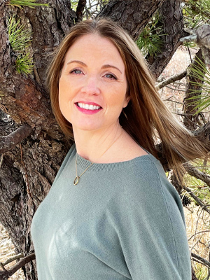 woman in green sweater standing in front of tree smiling