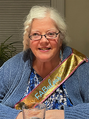 Woman with gold sash and blue cardigan smiling